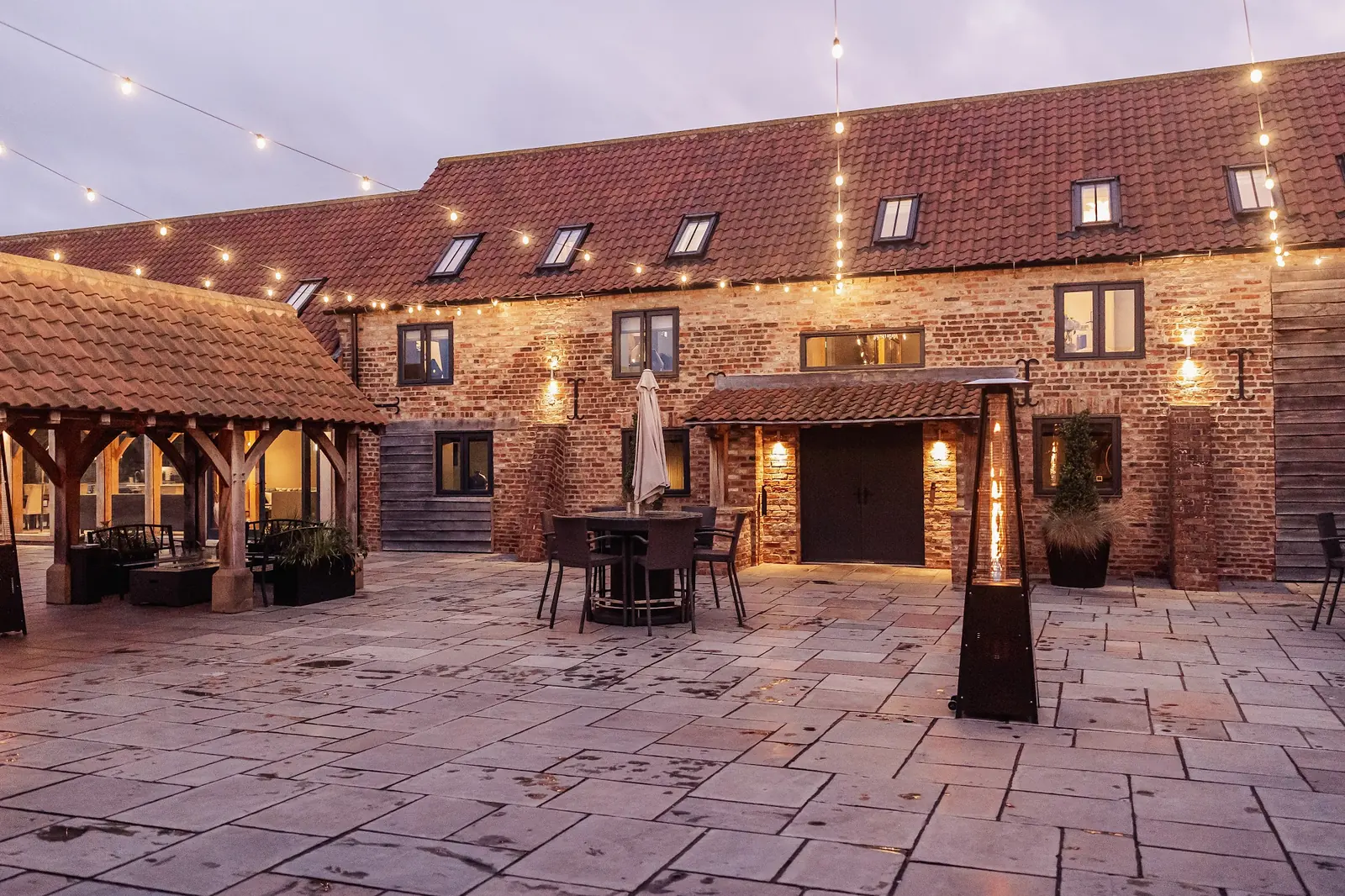 The courtyard at dusk under festoon lights, with outdoor heaters lit