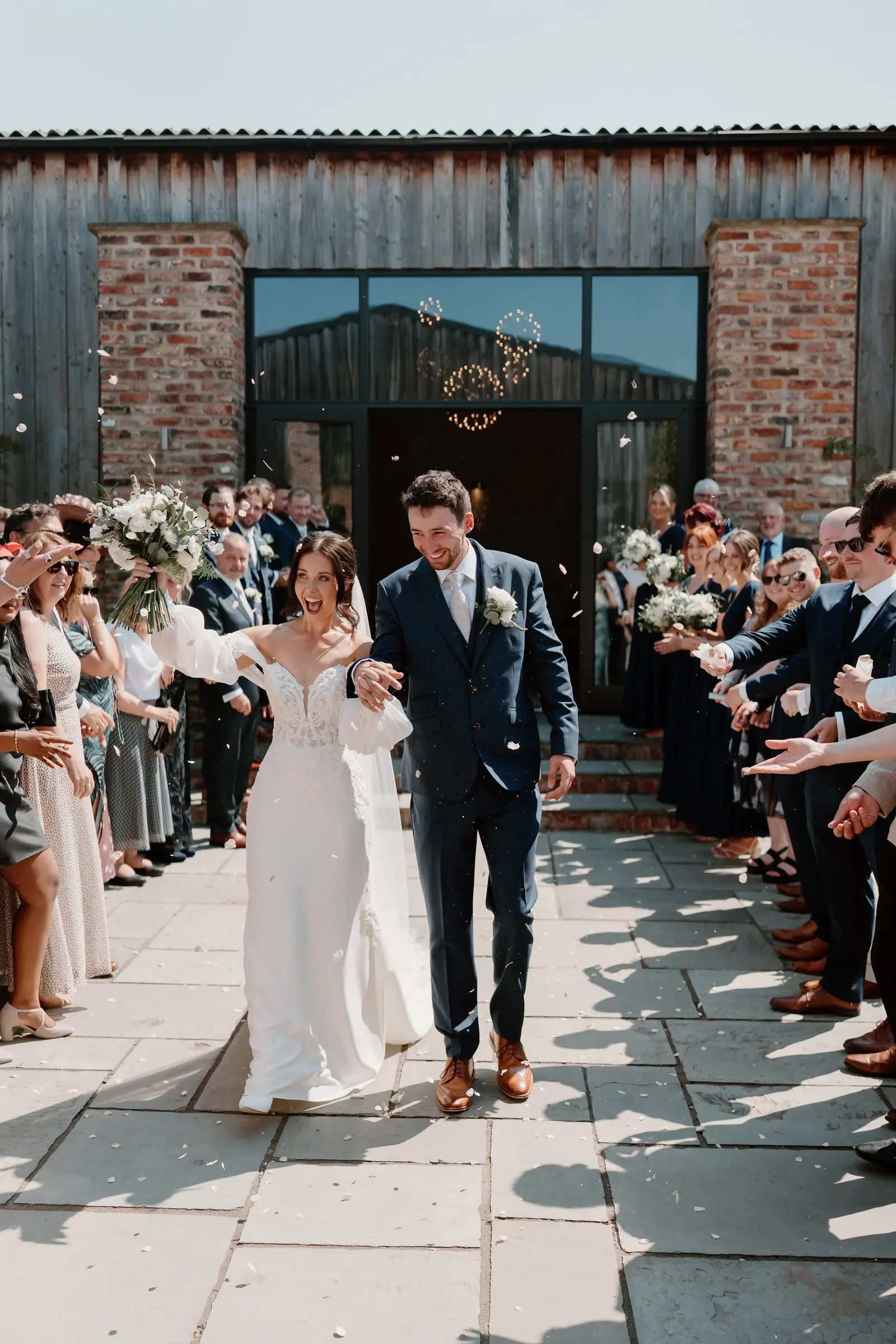A couple leaving the barn through a line of confetti