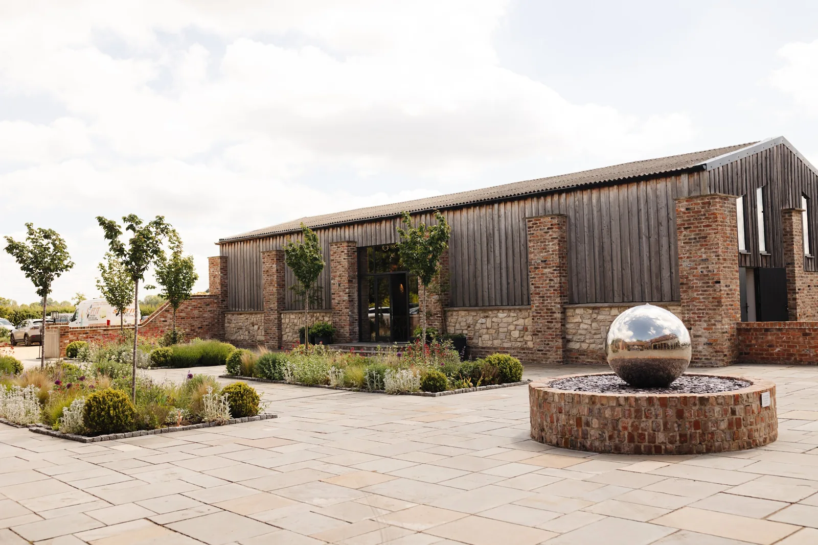 The Old Grain Store’s timber and brick walls behind the steel sphere water feature