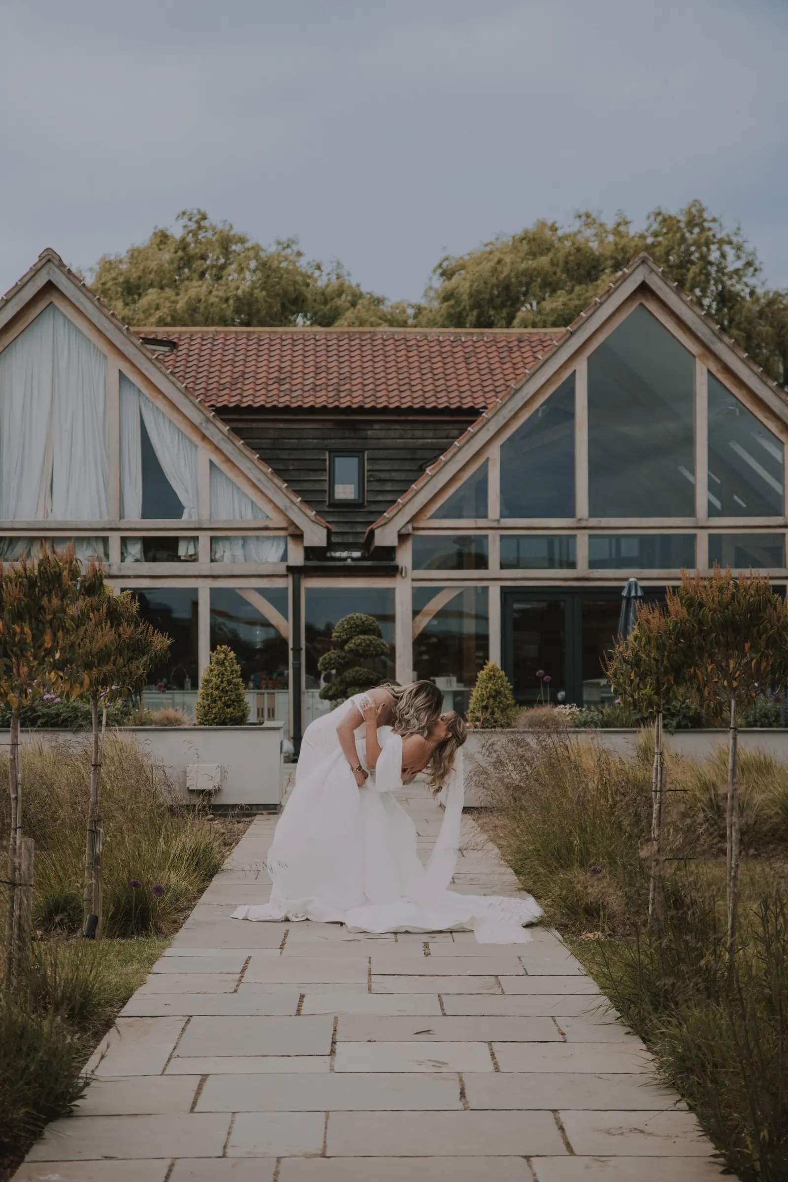 A bride on the stone path in front of the glass gables