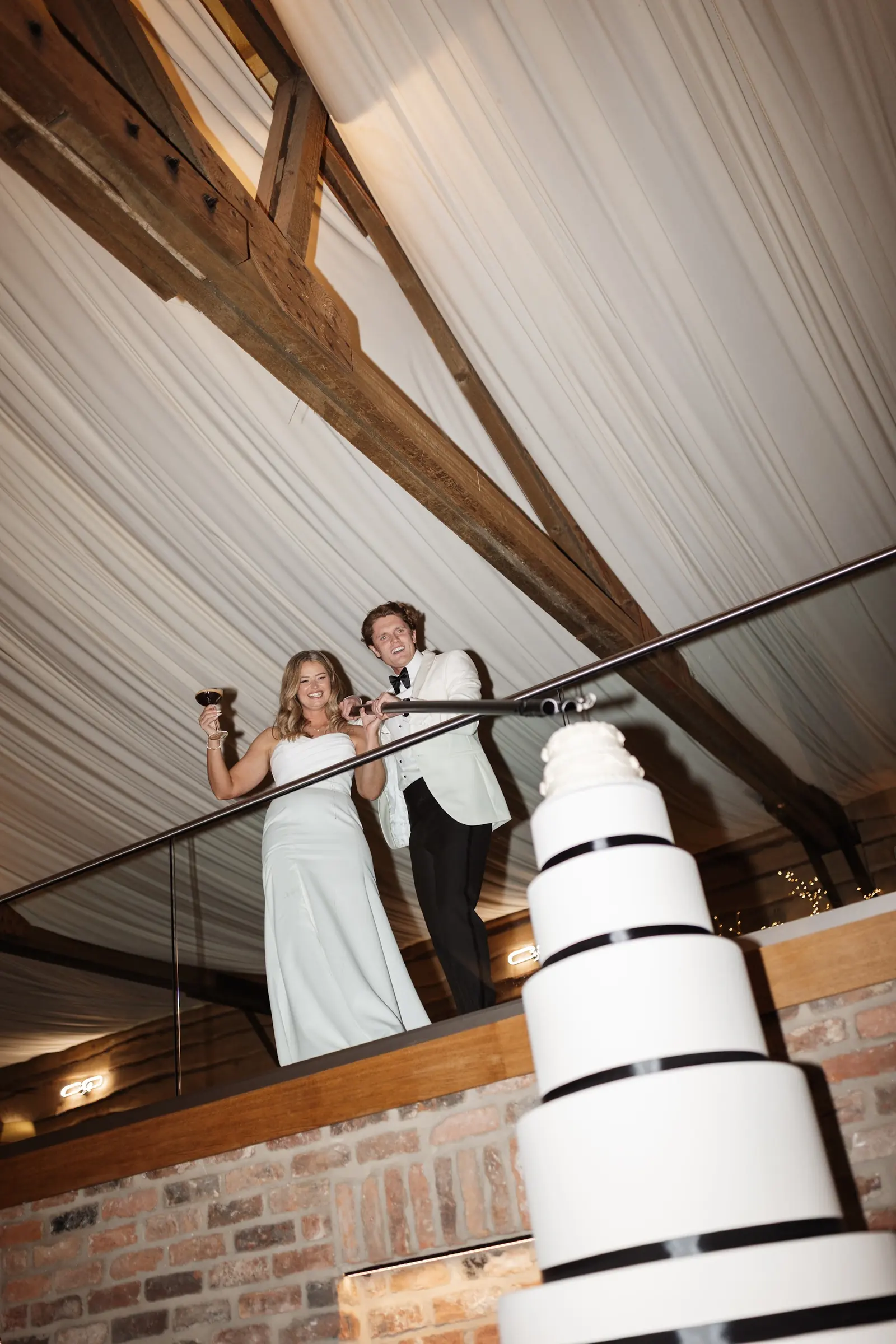 A couple on the mezzanine above the bar, beside a tall wedding cake