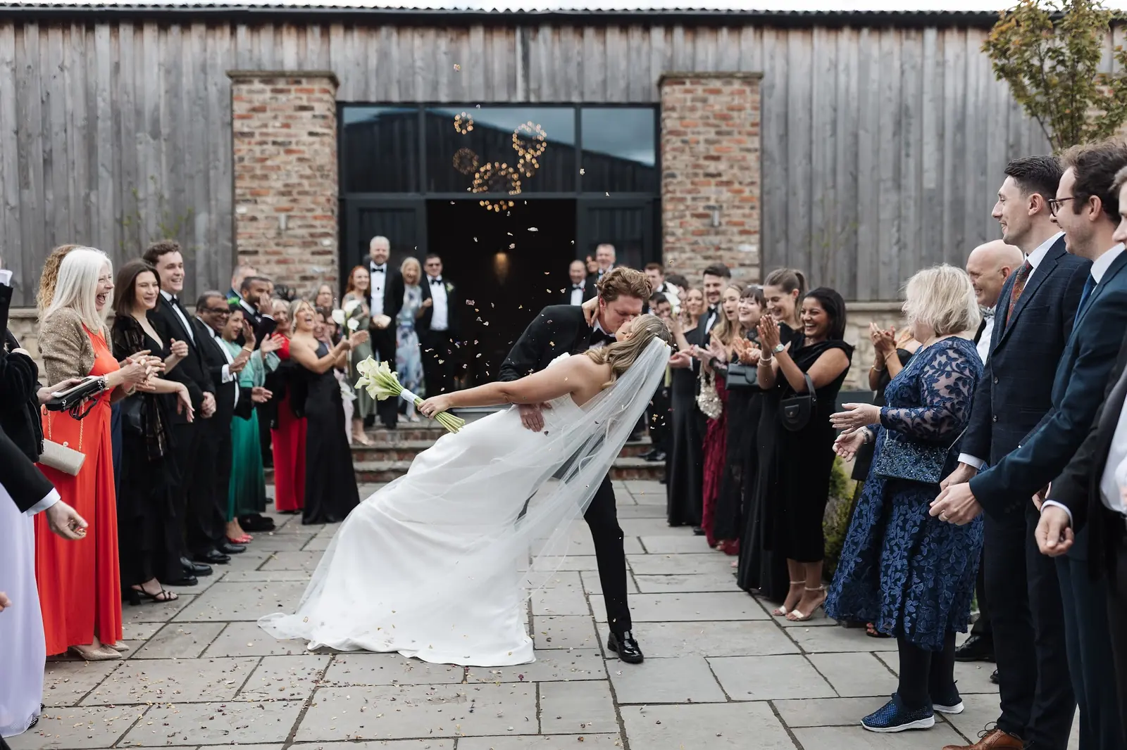 A groom dipping his bride in the courtyard as guests cheer