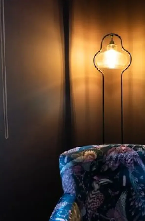 A glowing floor lamp beside a botanical print armchair