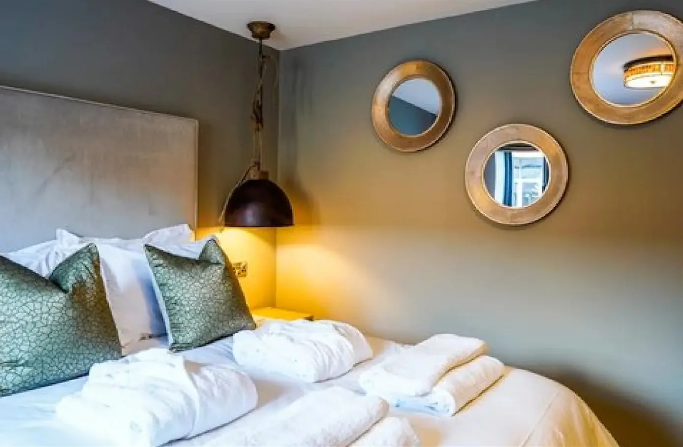 A bedroom with round brass mirrors above a grey headboard
