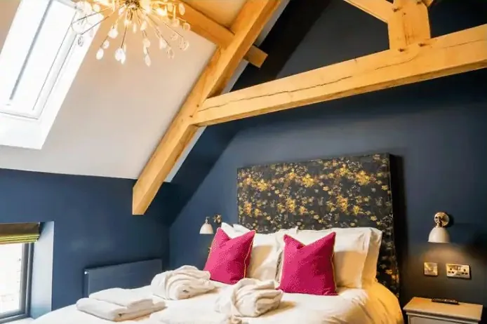 A bedroom under oak beams, with a navy wall and pink cushions