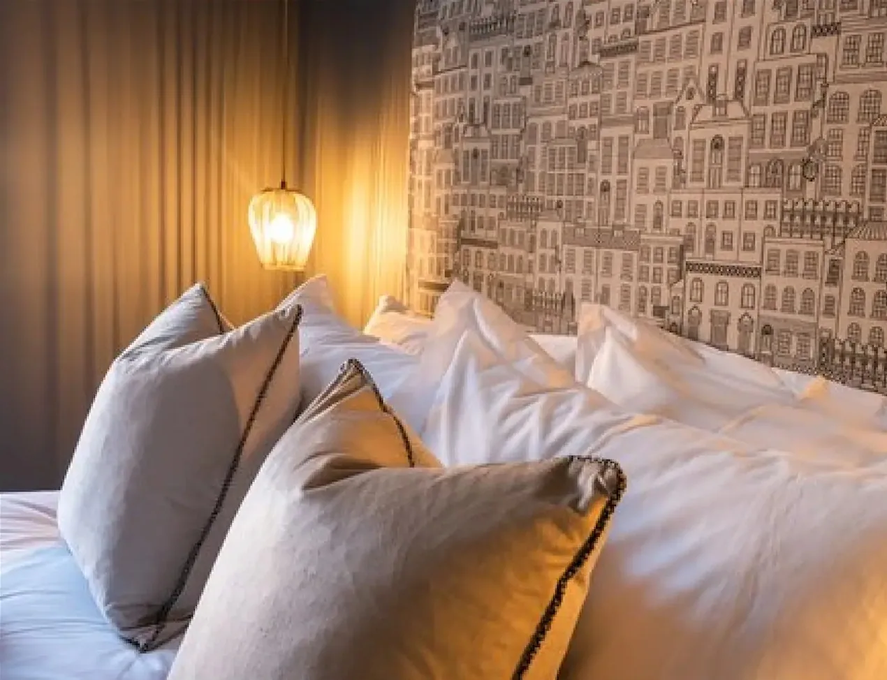 A bed dressed in white against a townhouse print wallpaper